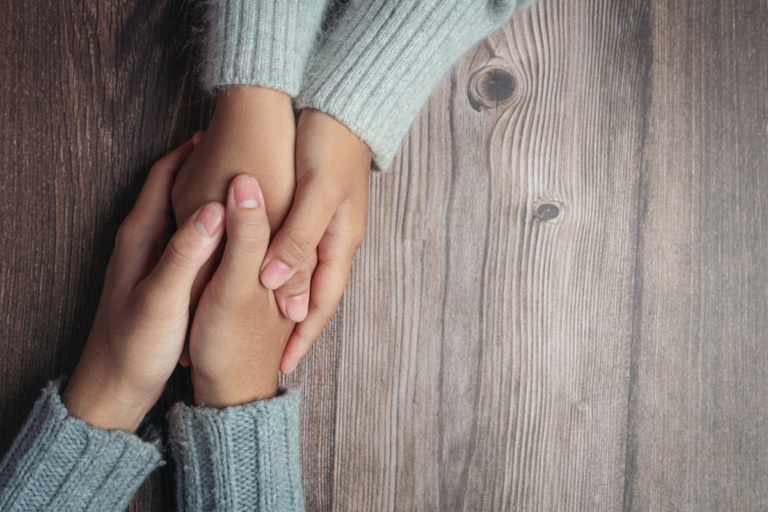 Two people holding hands together with love and warmth on wooden